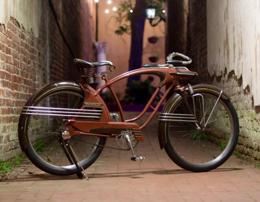Vintage red bicycle parked in a narrow alleyway with brick walls on both sides and soft lights in the background.
