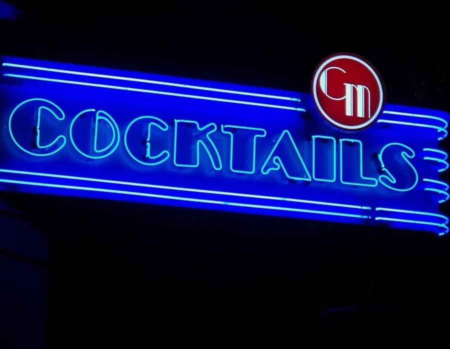 Neon blue sign displaying the word 'COCKTAILS' with a red and white circular logo on the top right.