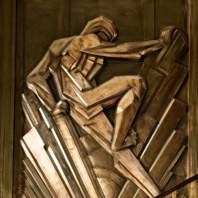 Bronze Art Deco relief of a geometric human figure in a dynamic pose, made of angular metallic shapes.