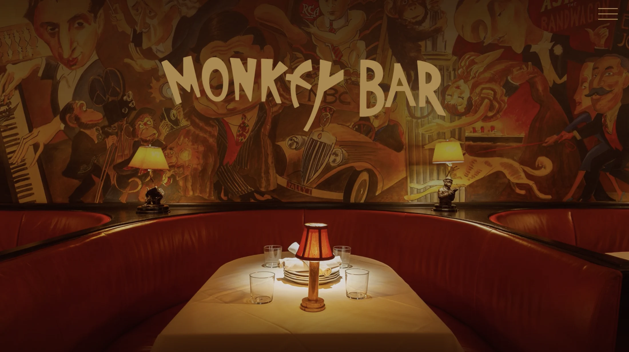 Interior of a bar with a curved red leather booth, a table lamp, and artistic mural on the wall with the words 'Monkey Bar'