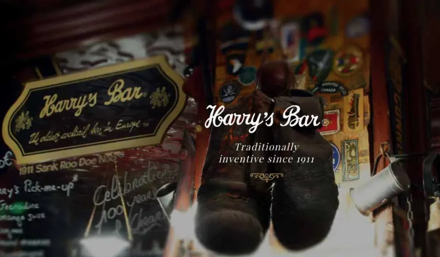Interior view of Harry's Bar with hanging boots and decorative patches on the wall, featuring the sign Harry's Bar and the text traditionally inventive since 1911.
