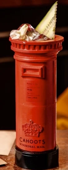 Red cylindrical cocktail glass designed like a British post box with ice cubes and a cucumber slice garnish