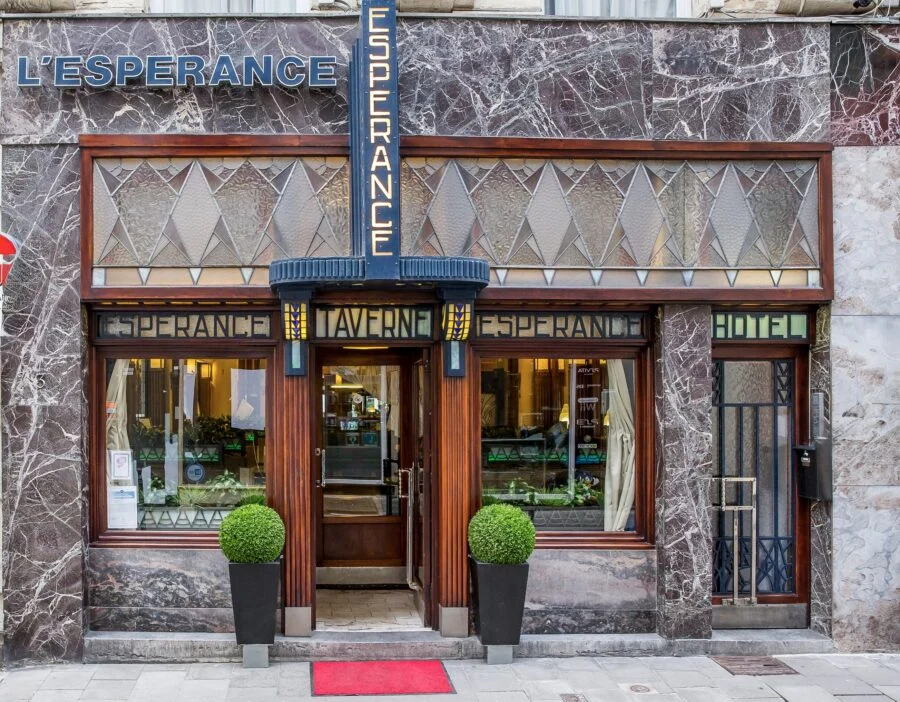 Exterior view of L'Esperance, a vintage-style hotel and tavern entrance with stone facade and stained glass windows.