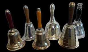 Row of six polished handbells with wooden and metal handles on a black background