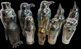 Collection of vintage metal cocktail shakers, many shaped like penguins, on a black background