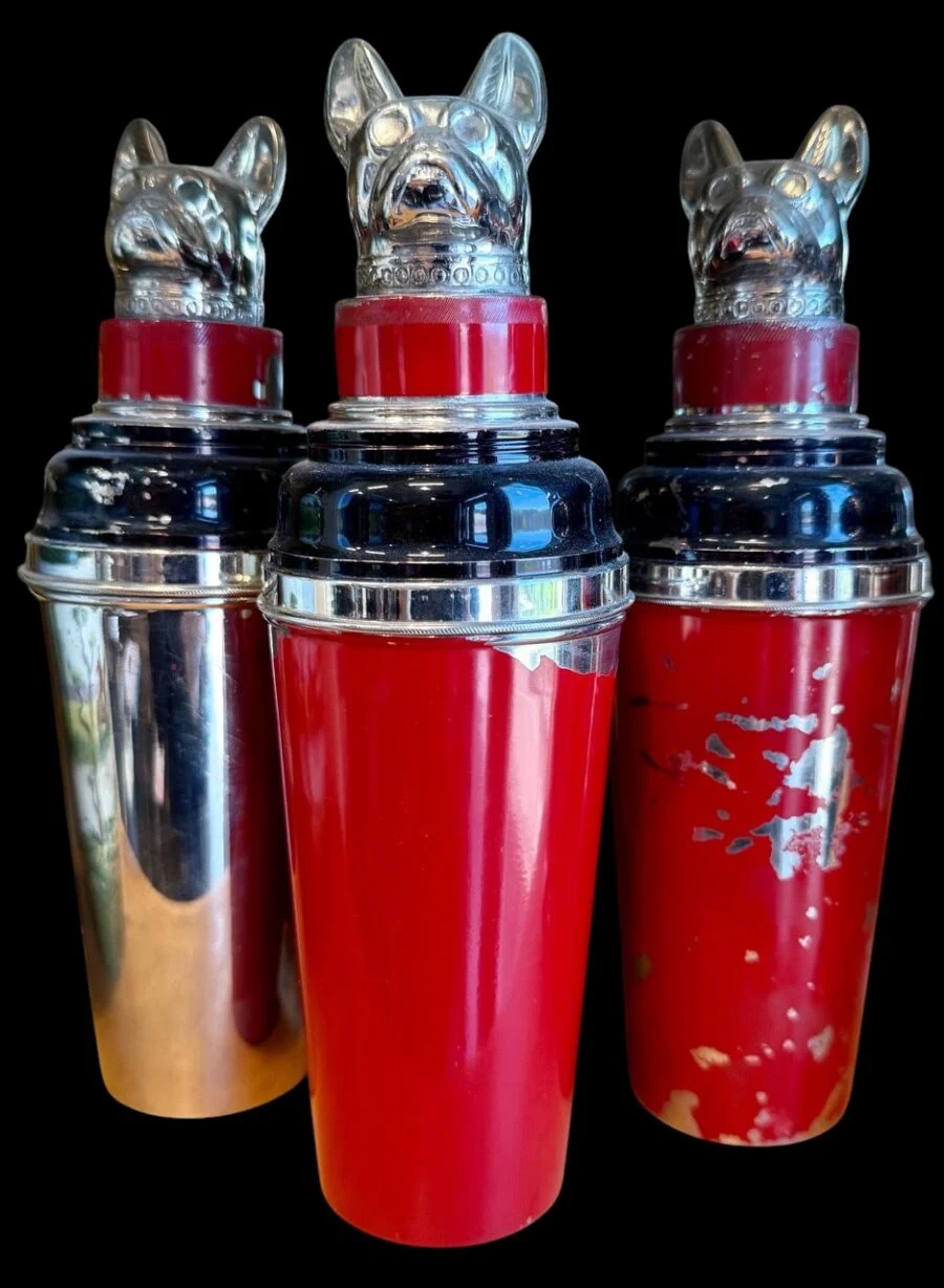 Three vintage cocktail shakers with metallic dog-head lids on a black background