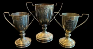 Three vintage silver trophy cups on a black background