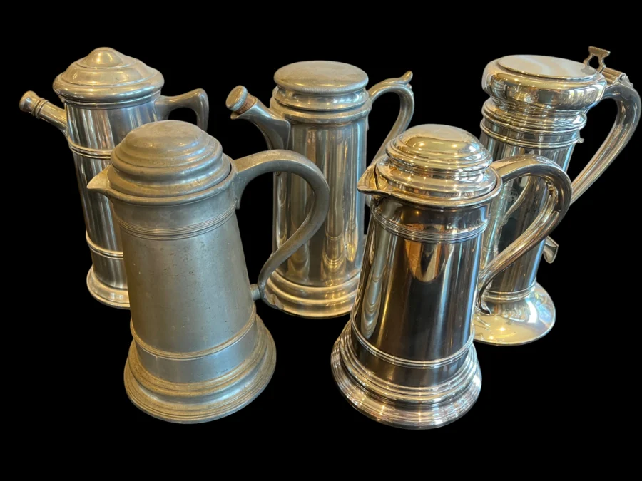 Group of five vintage metal tankards with lids on a black background