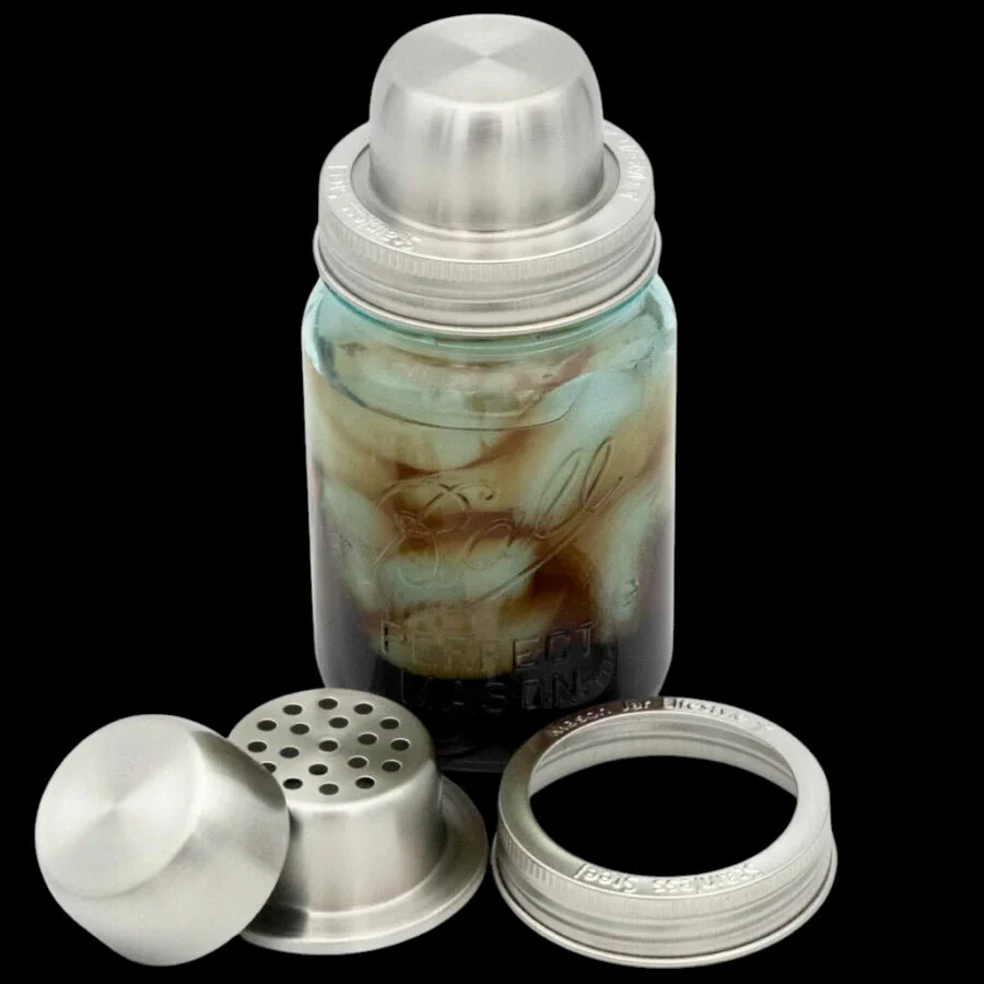 Stainless steel cocktail shaker lid set on a mason jar with iced drink