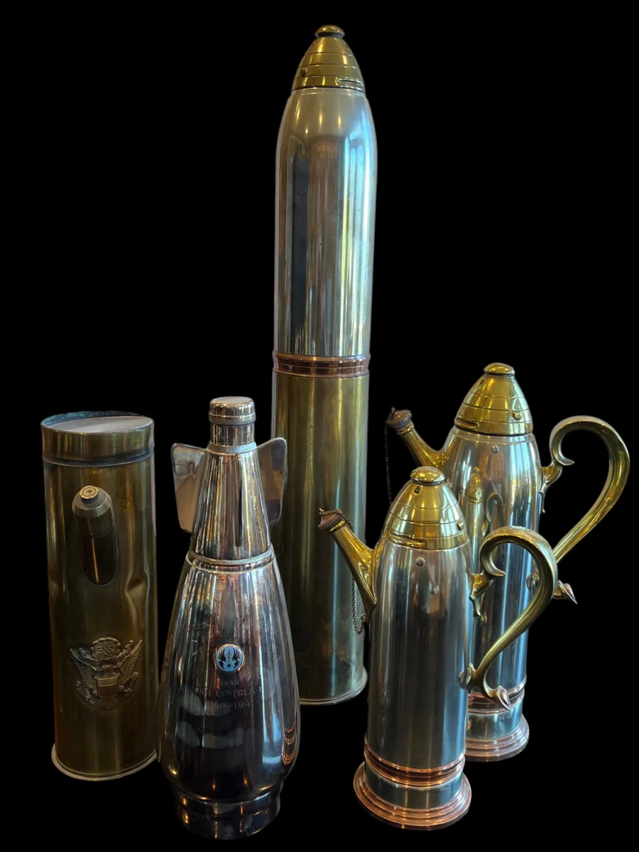 Collection of polished metal artillery shell casings repurposed as decorative pitchers and containers against a black background