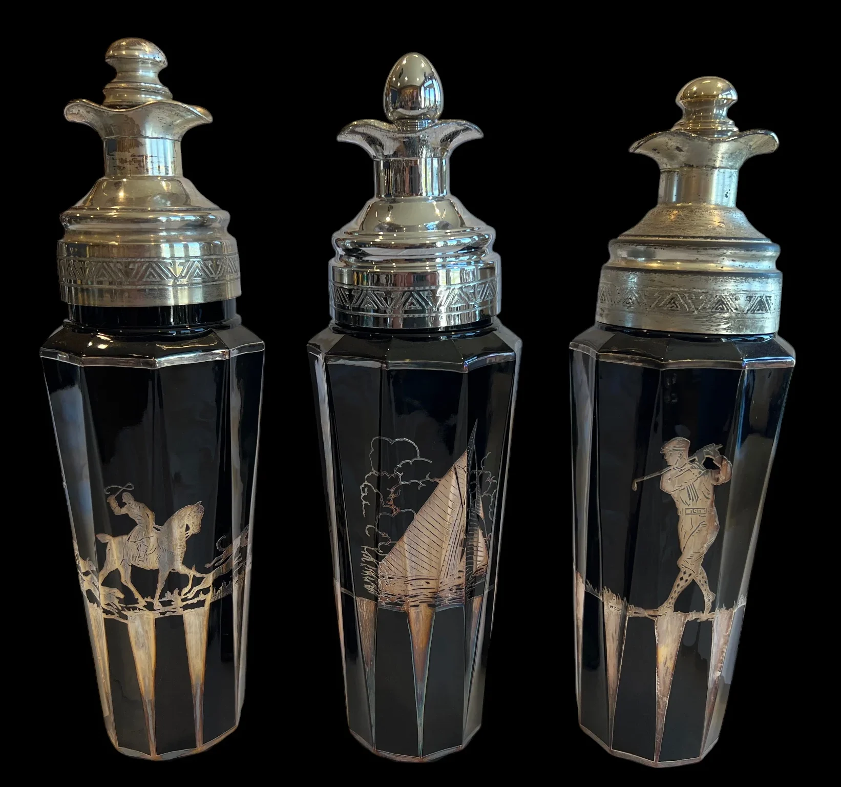 Three black glass cocktail shakers with silver tops and etched sporting scenes