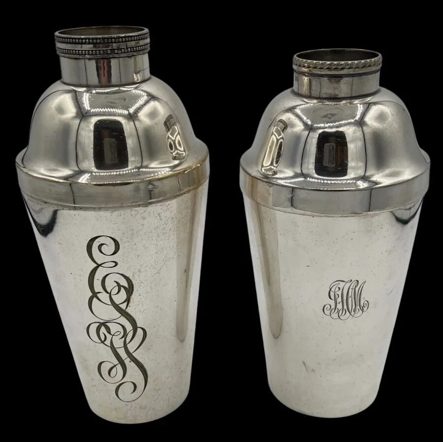 Two vintage silver cocktail shakers with engraved monograms on a black background
