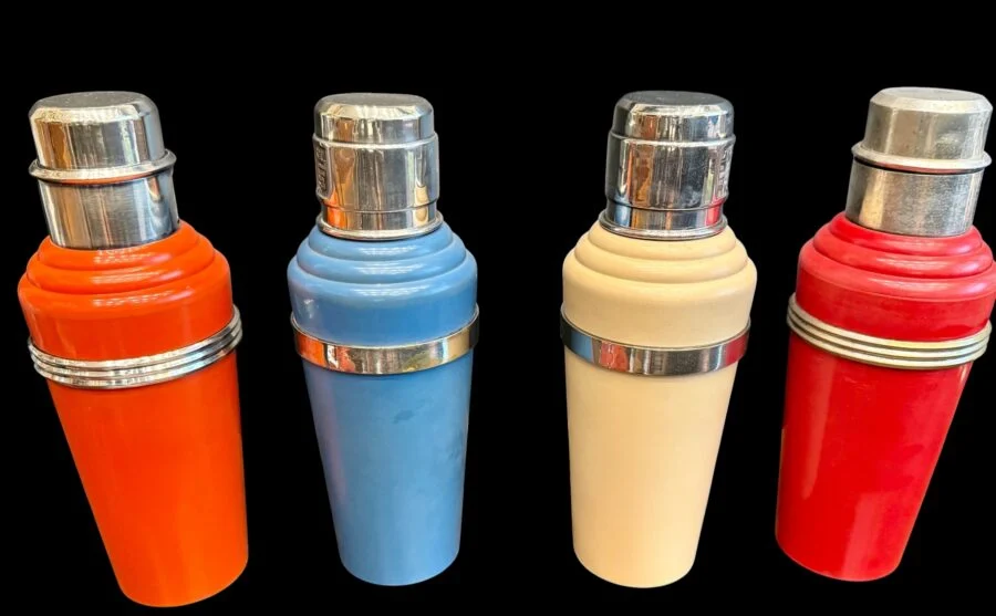 Four colorful vintage cocktail shakers with chrome tops on a black background