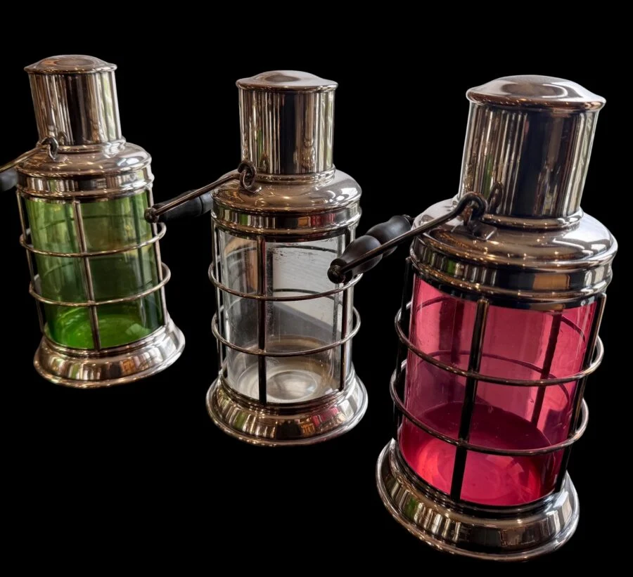 Three metal lanterns with green, clear, and red glass on a black background