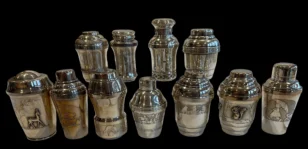 Collection of vintage metal cocktail shakers with engraved and illustrated designs on a black background
