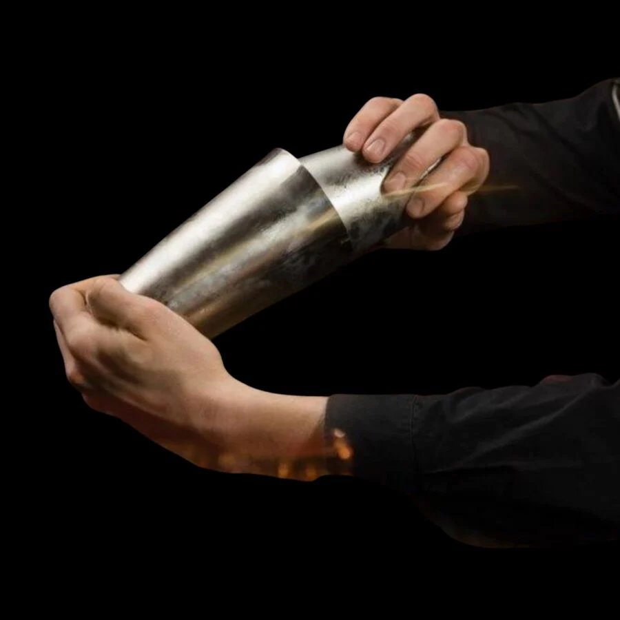 Bartender shaking a stainless steel cocktail shaker against a black background