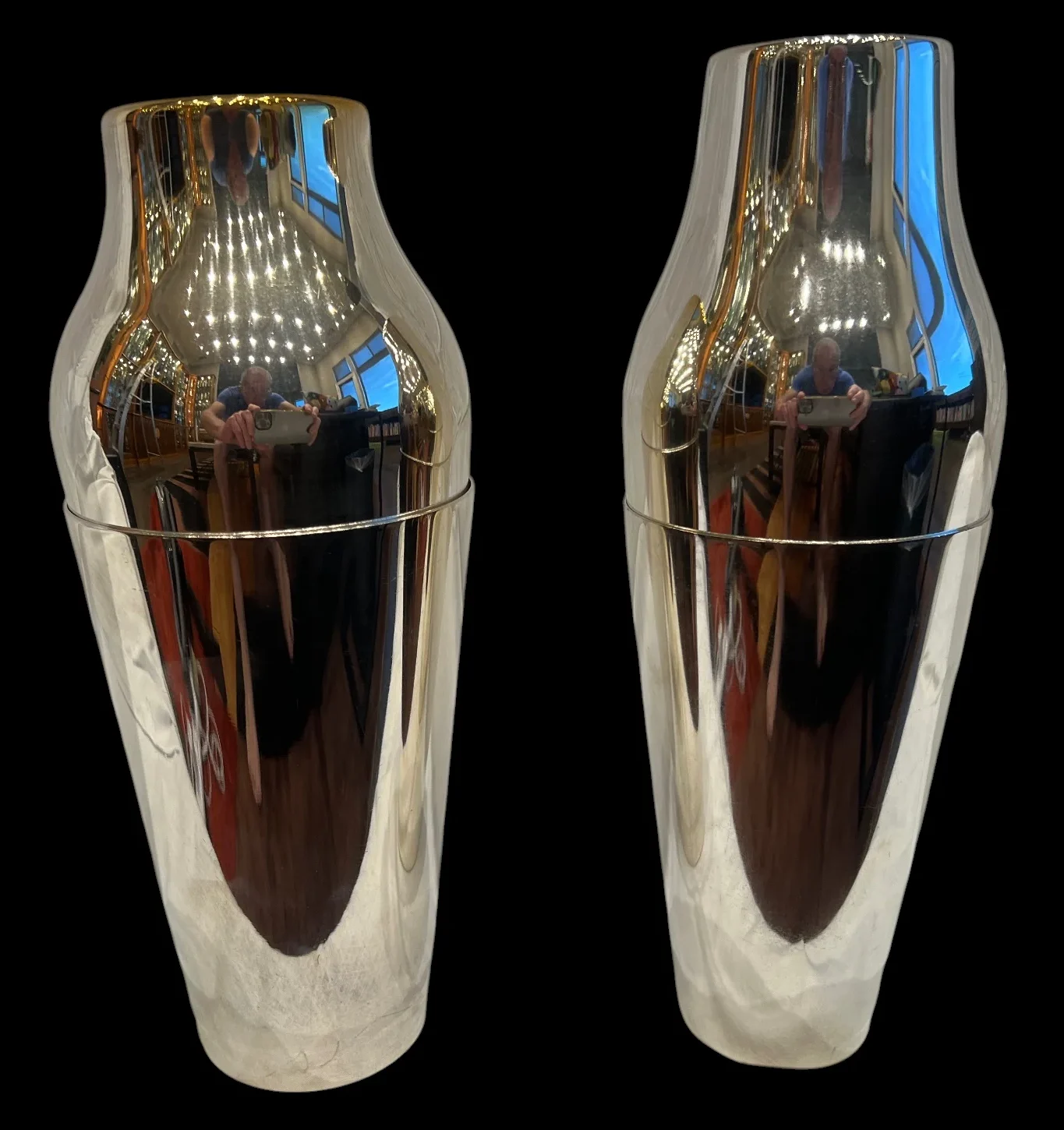 Two reflective stainless steel cocktail shakers against a black background