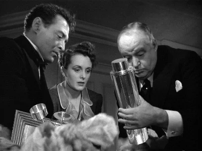 Black and white scene of three people examining a metallic object closely, dressed in formal attire.