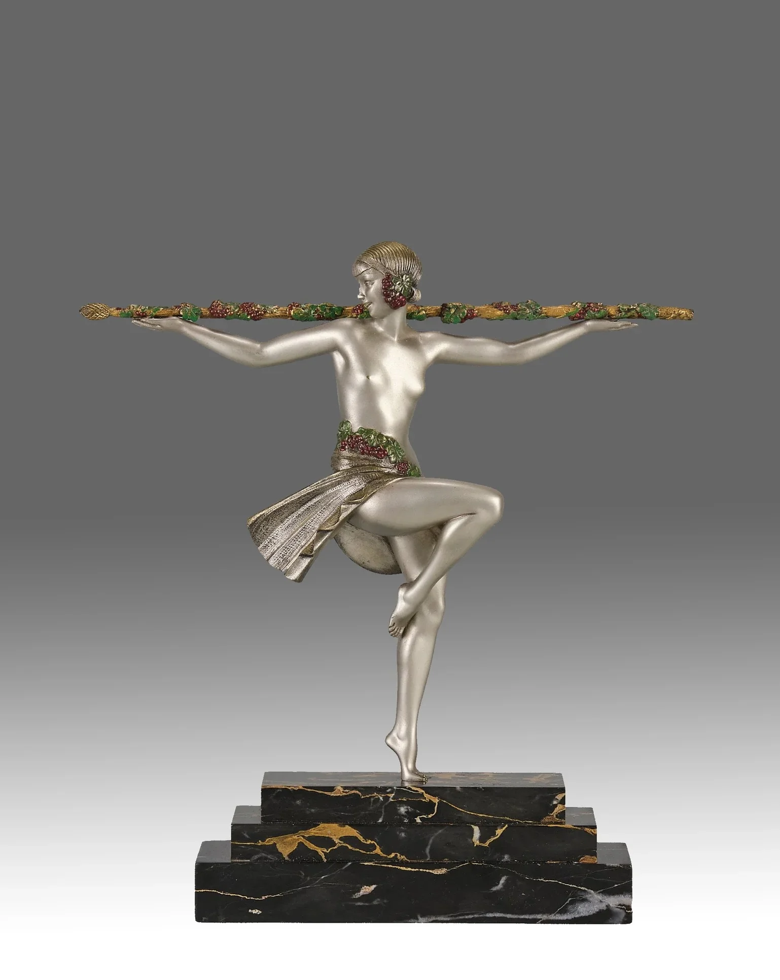 Art deco sculpture of a female figure balancing on one foot on a stepped black marble base, holding a decorative staff horizontally with both hands.