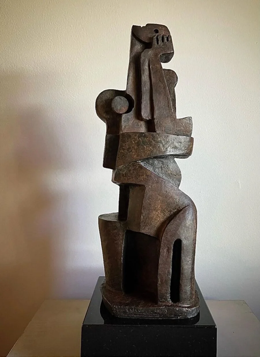 abstract bronze sculpture of a seated figure on a dark pedestal