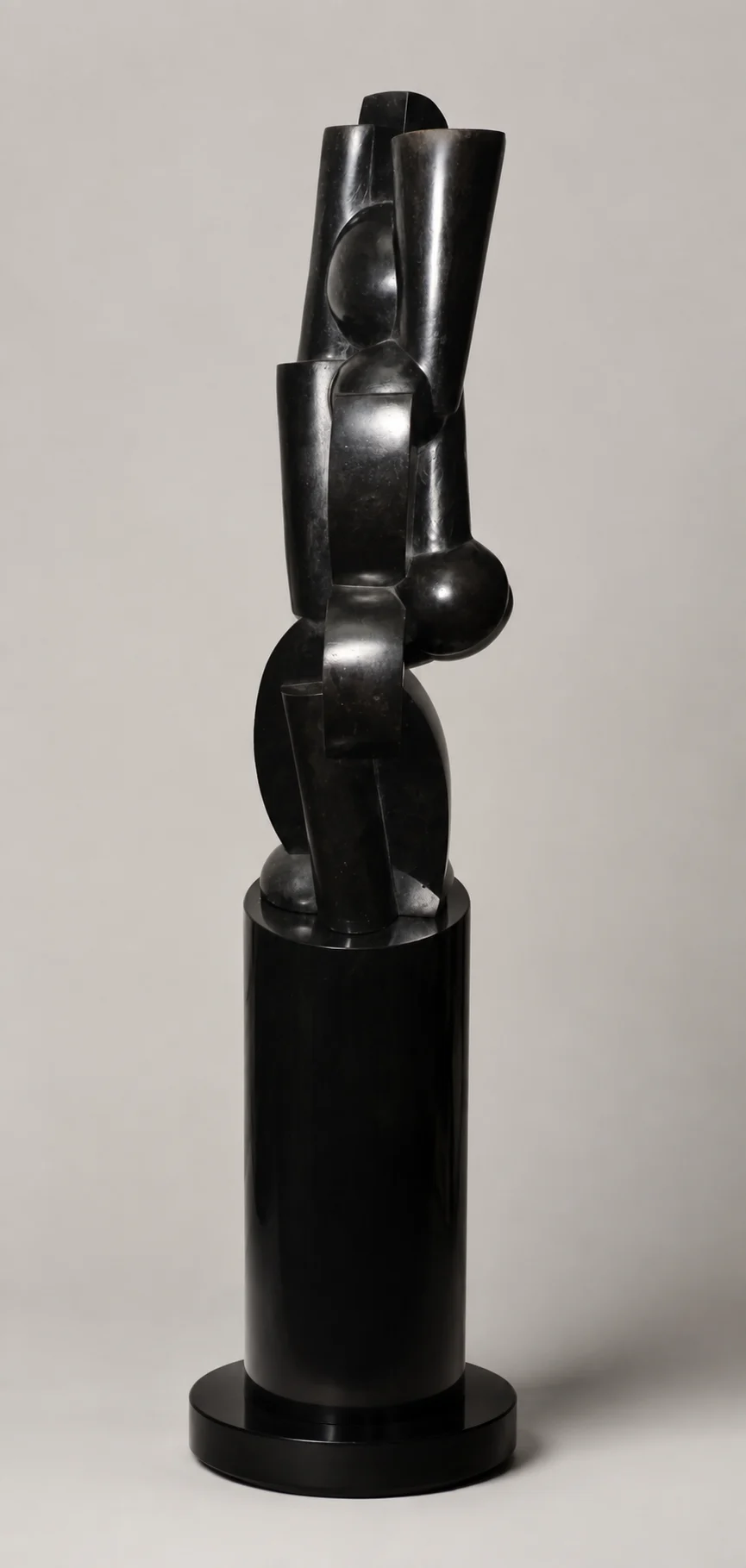 Abstract black metal sculpture composed of cylindrical and geometric forms on a tall pedestal