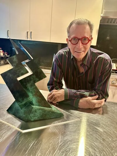Man with red glasses posing beside abstract green metal sculpture in modern kitchen