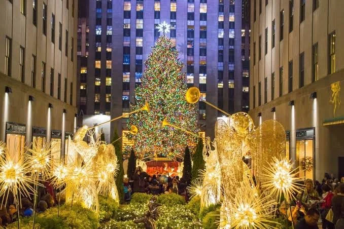 Nighttime view of a large decorated Christmas tree surrounded by golden angel and star lights in a city plaza