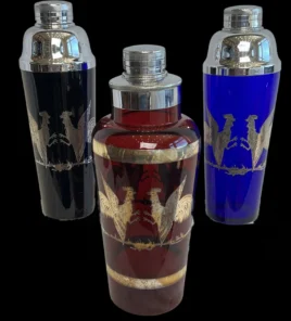 Three vintage cocktail shakers with silver rooster engravings on black, red, and blue glass