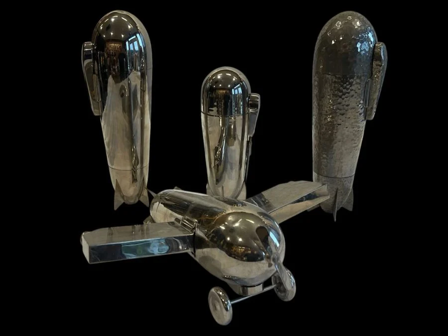 shiny metal airplane sculpture with three standing rocket-shaped pieces on black background