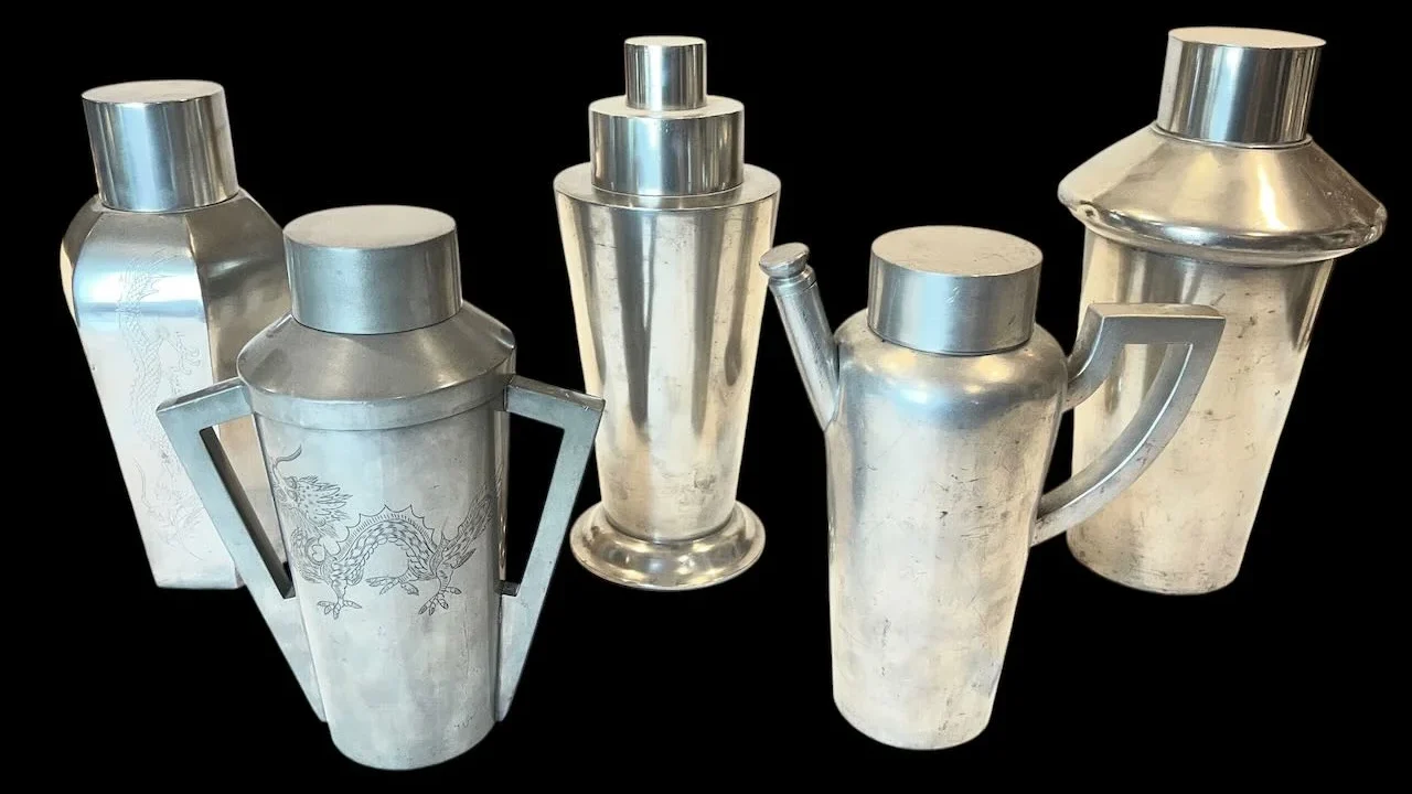 Five vintage metal cocktail shakers on a black background