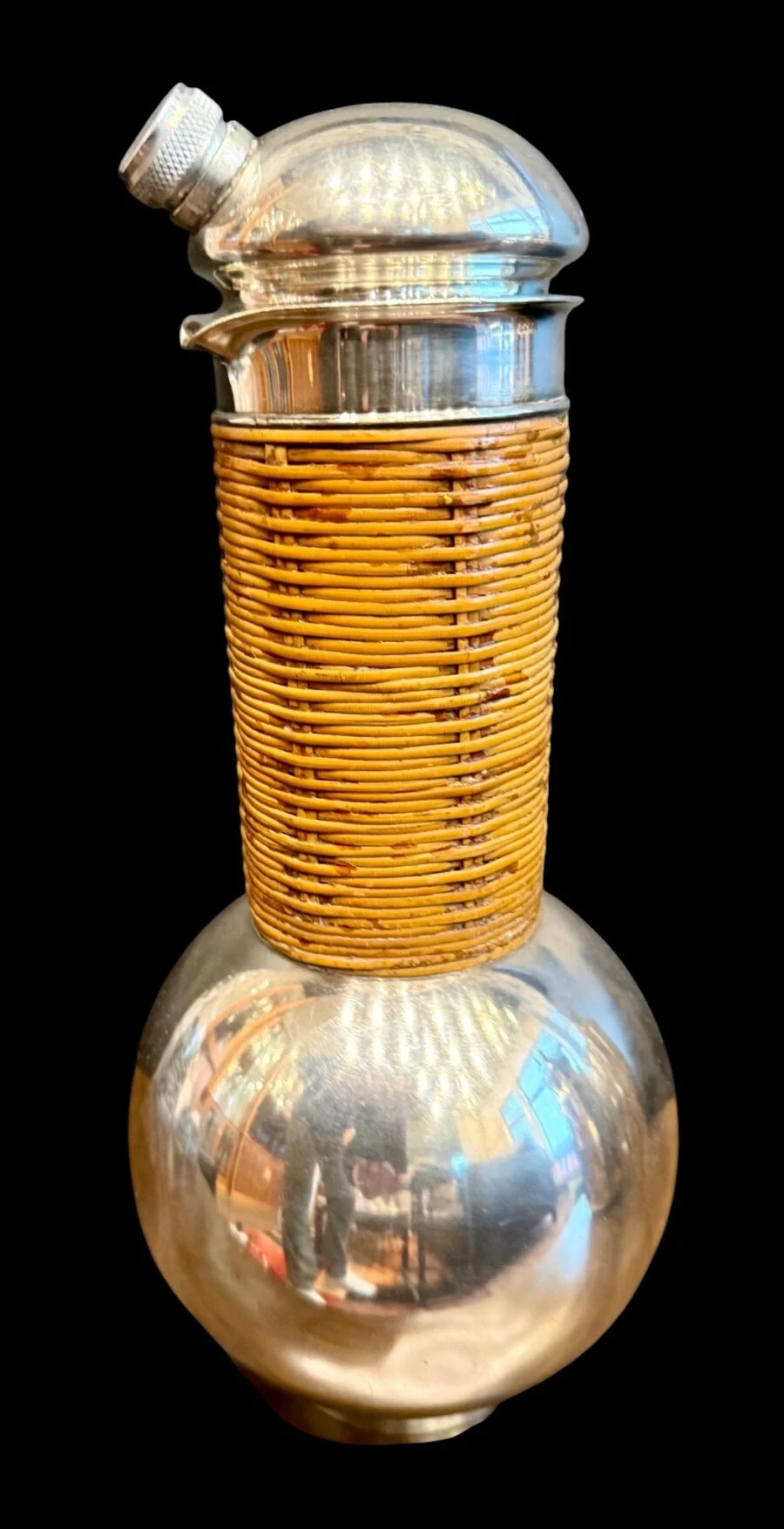 Vintage metal flask with woven wicker middle section on black background