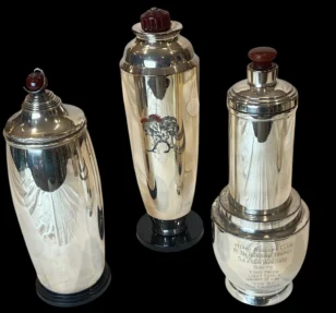 Three vintage silver cocktail shakers standing against a black background