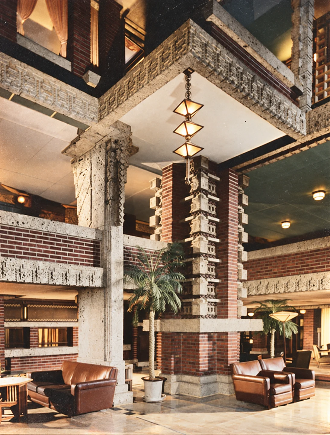 Interior of a grand lobby with brick and concrete columns, leather seating, and geometric pendant lights