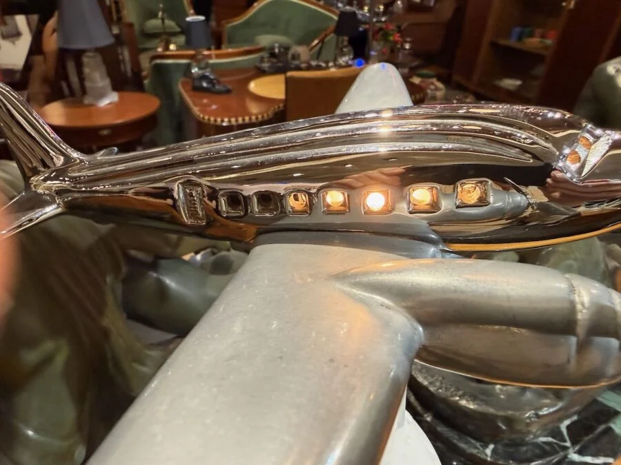Close-up of a chrome airplane sculpture with illuminated windows held by a stylized metallic figure