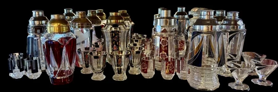 Collection of vintage glass cocktail shakers and matching glasses on a black background
